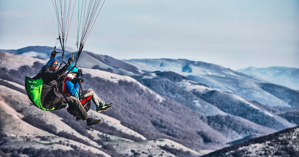 Volo in parapendio biposto con sfondo montagne di Norma